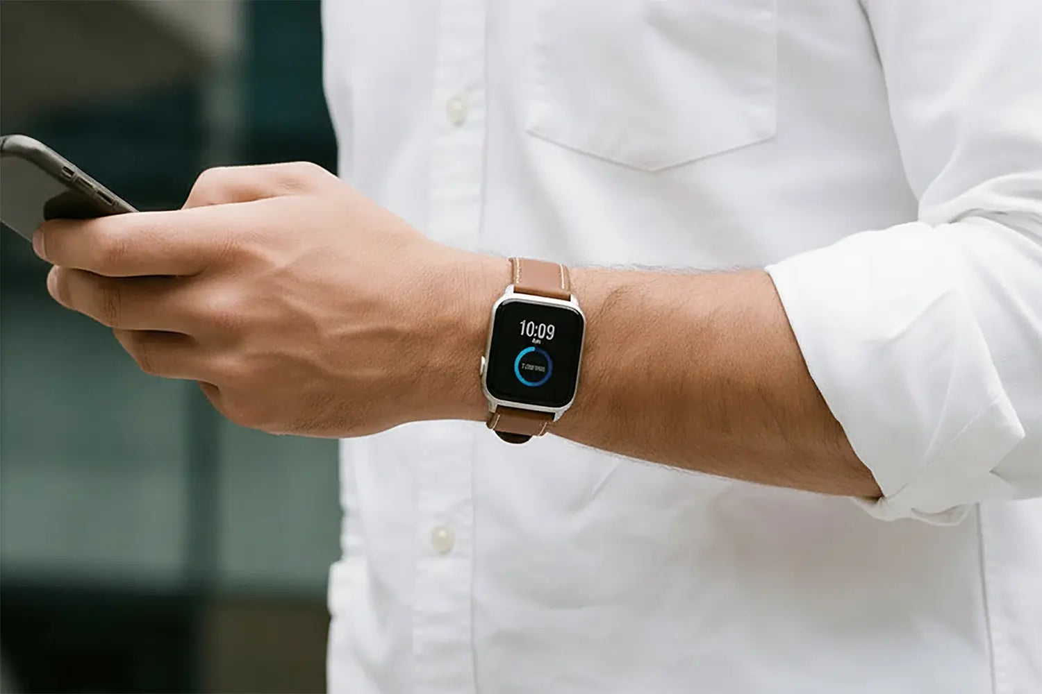 Person wearing a smartwatch and using a phone, with a blurred background