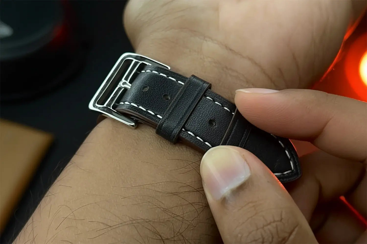 Close-up of a wrist wearing a black leather watch strap with a silver buckle.