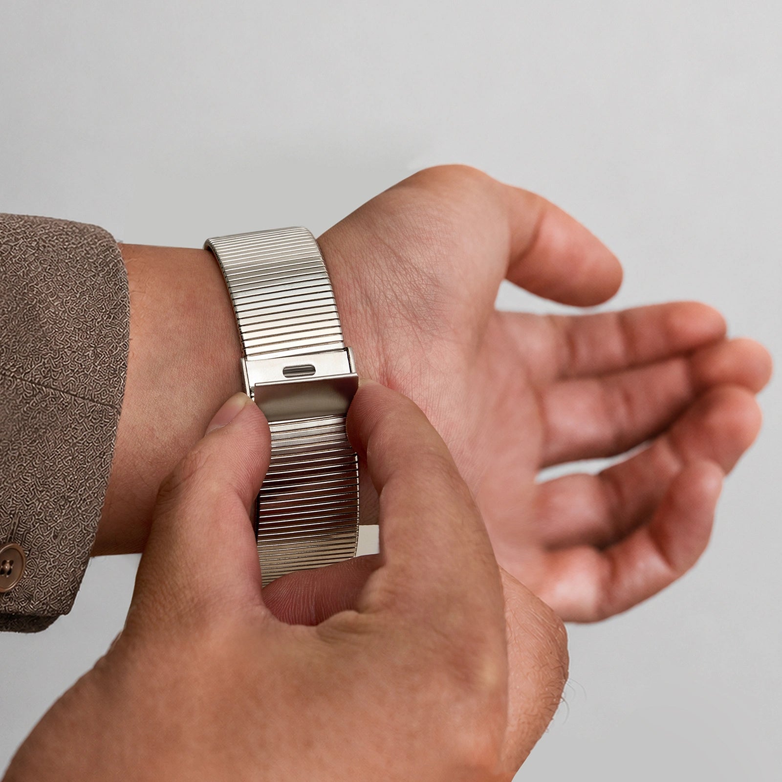 Close-up of a hand wearing a silver watch with a textured band on a neutral background