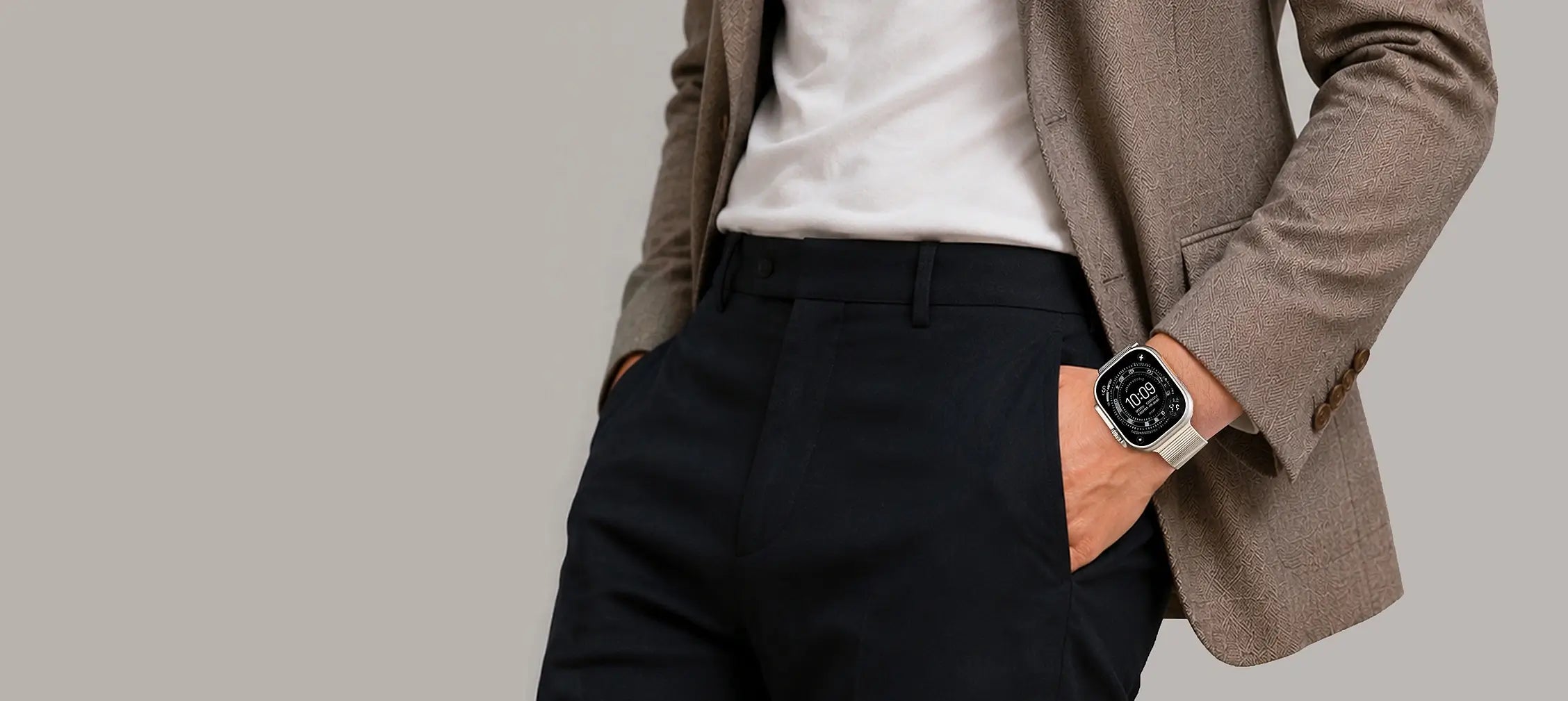 Person wearing a brown blazer and black pants with a watch on a gray background