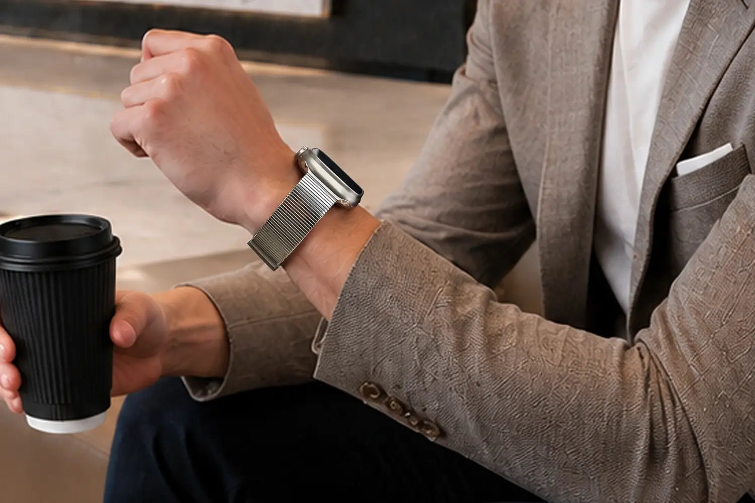 Person holding a black coffee cup with a watch on wrist, wearing a brown suit.