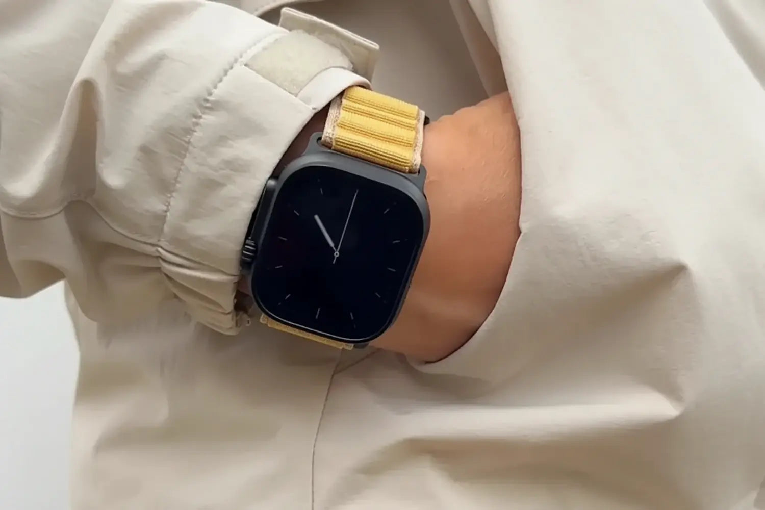 Smartwatch with a gold band on a person's wrist, wearing a light-colored jacket.