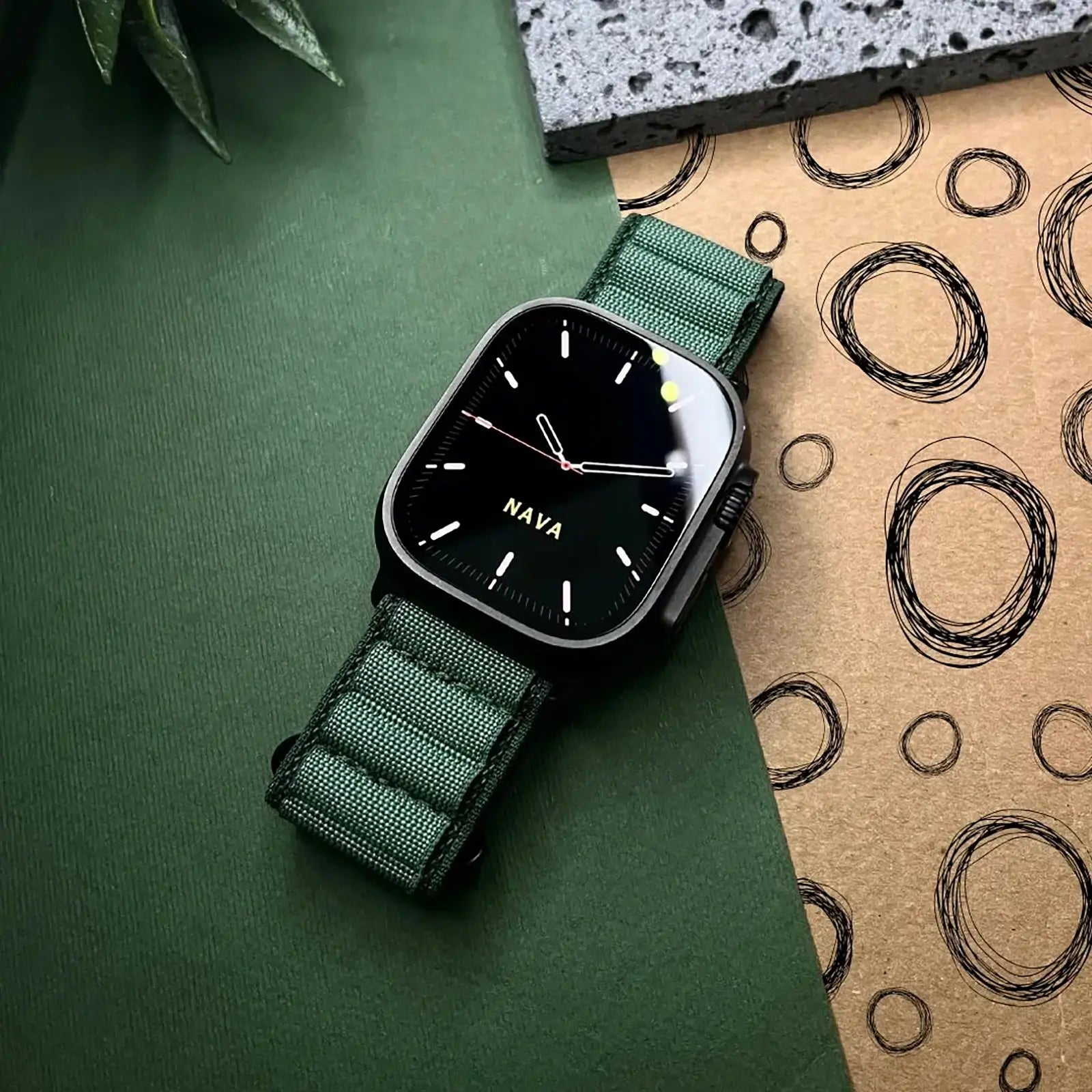 Watch with green strap on a green surface with a cardboard box in the background