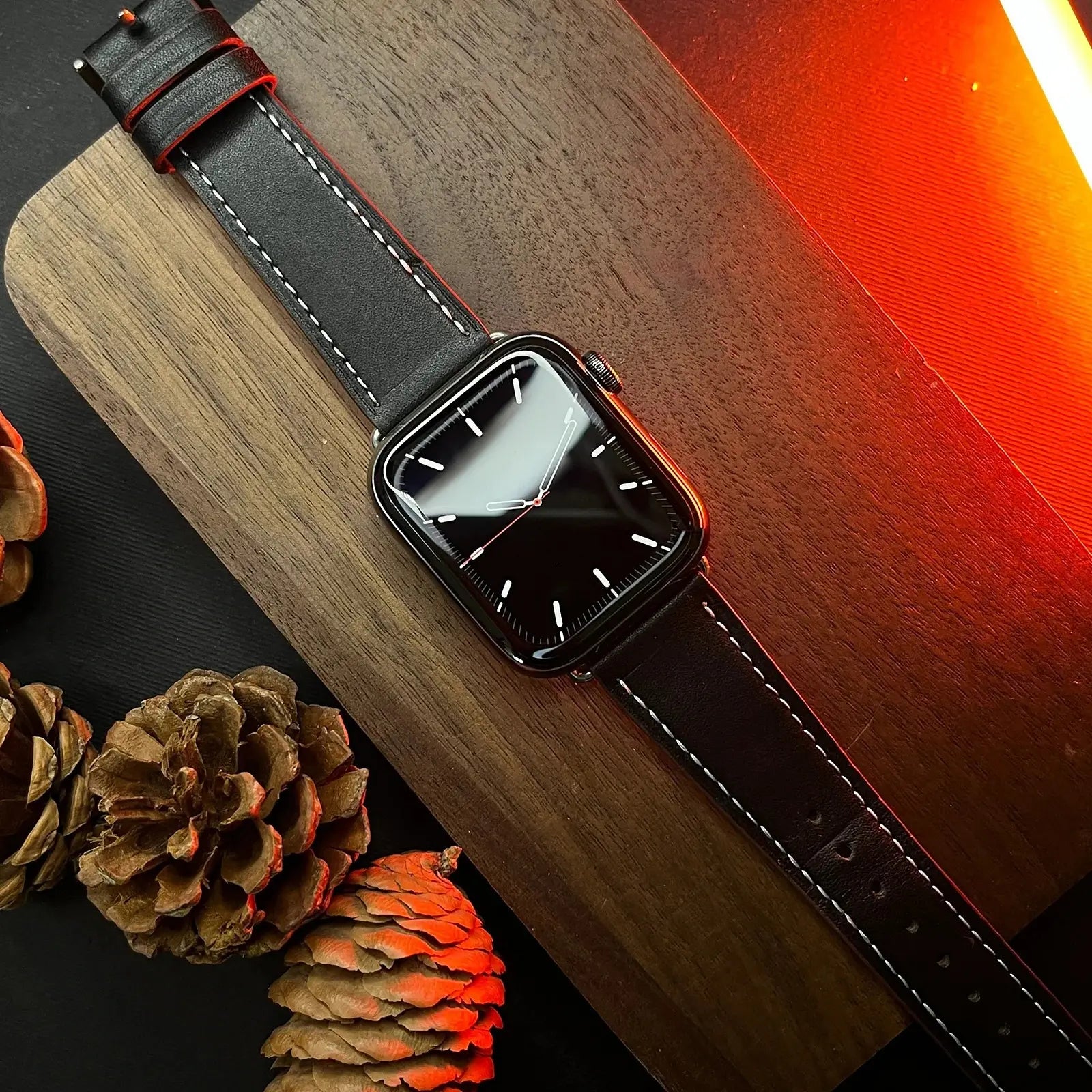 Smartwatch with a black strap on a wooden surface with pine cones.