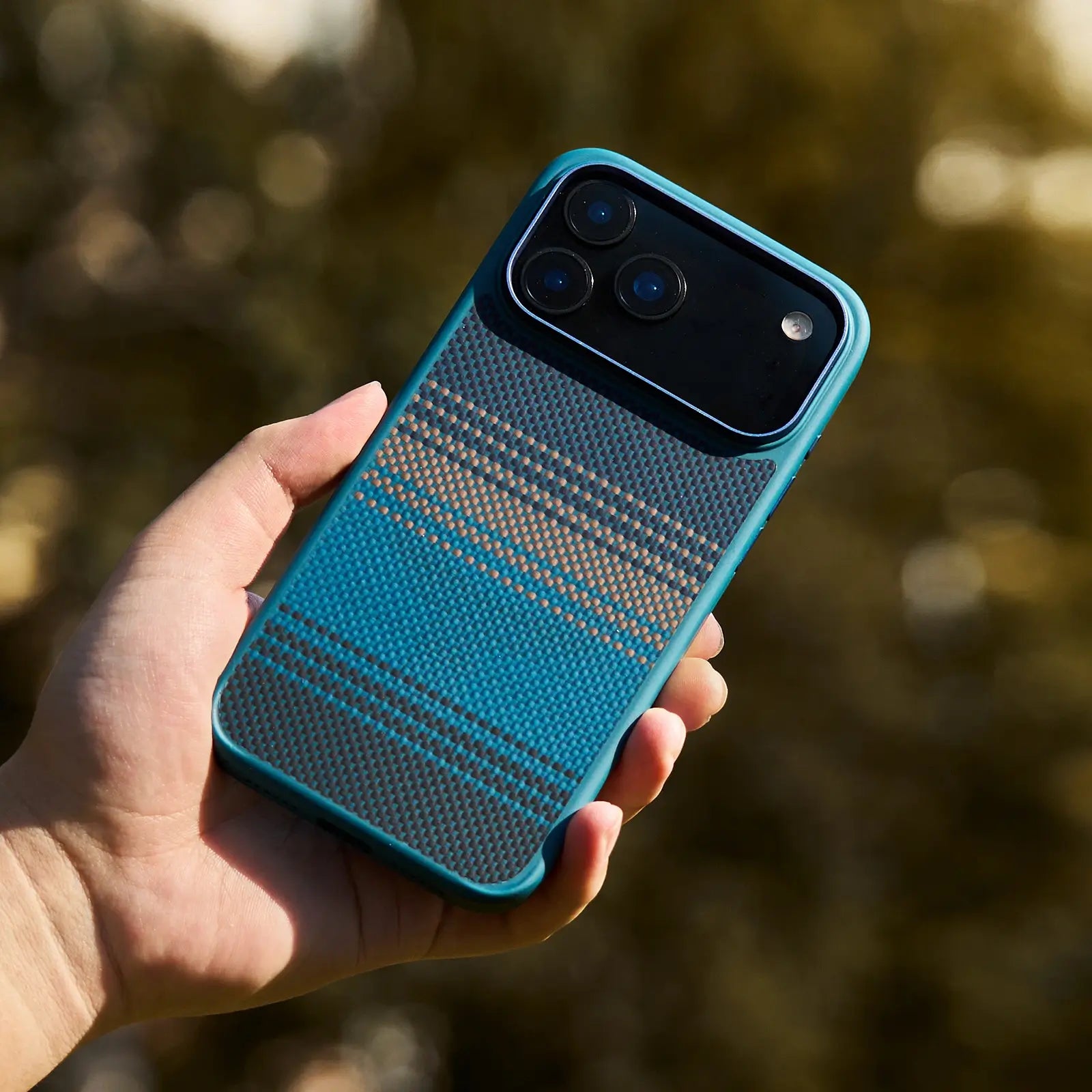 Hand holding a blue phone case with a textured pattern against a blurred natural background