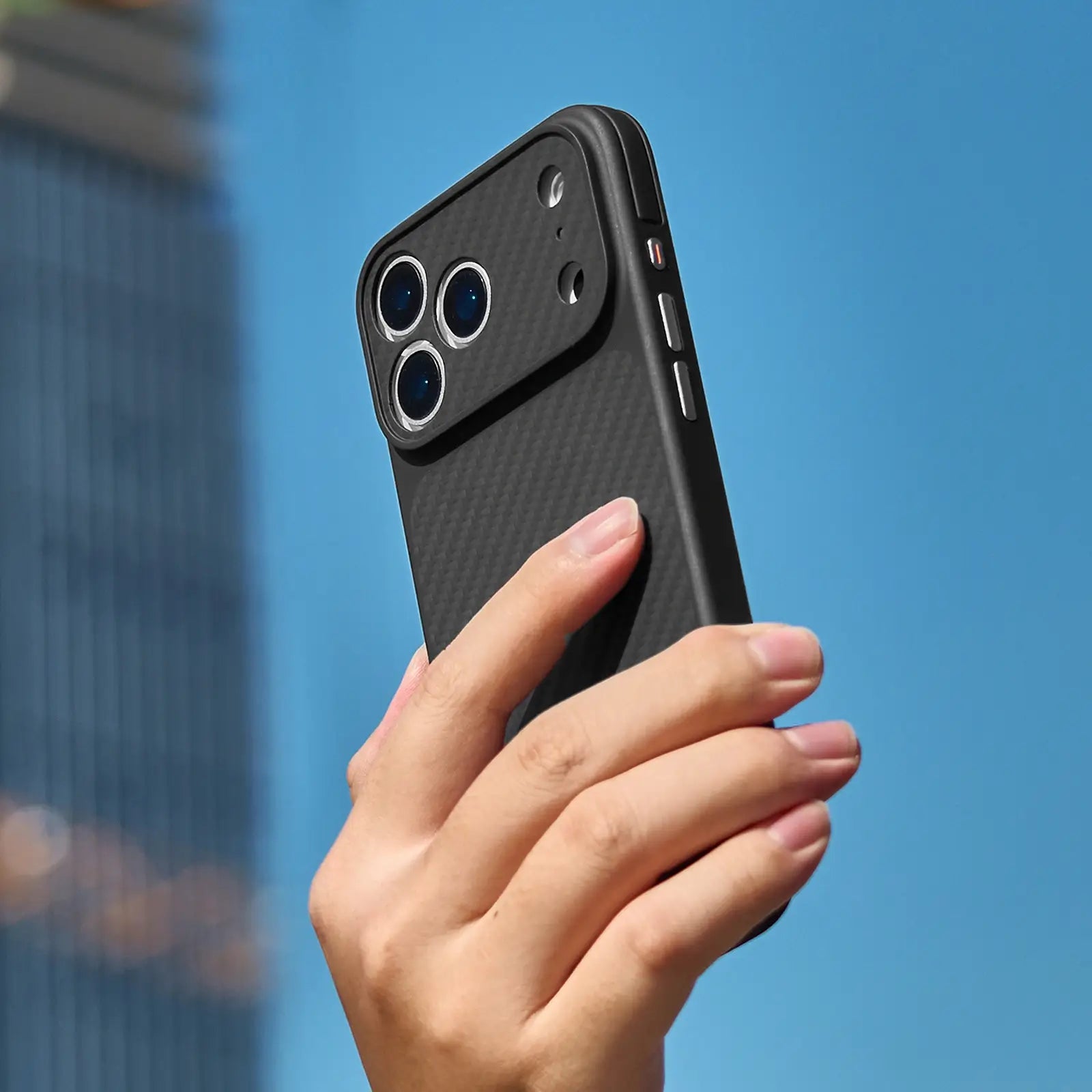 Hand holding a black phone case against a blue sky
