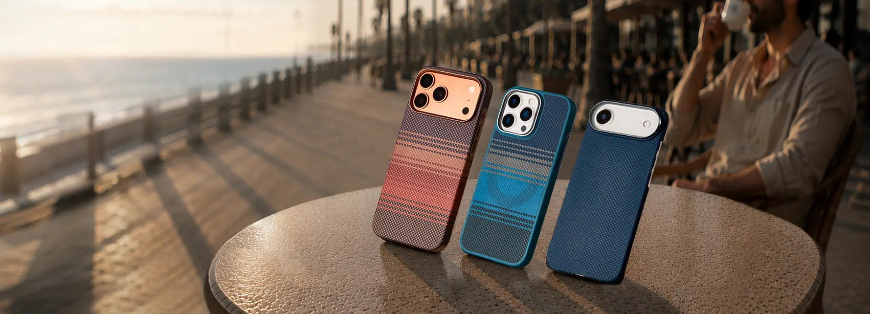 Three gradient-colored phone cases on a table with a beach and person in the background