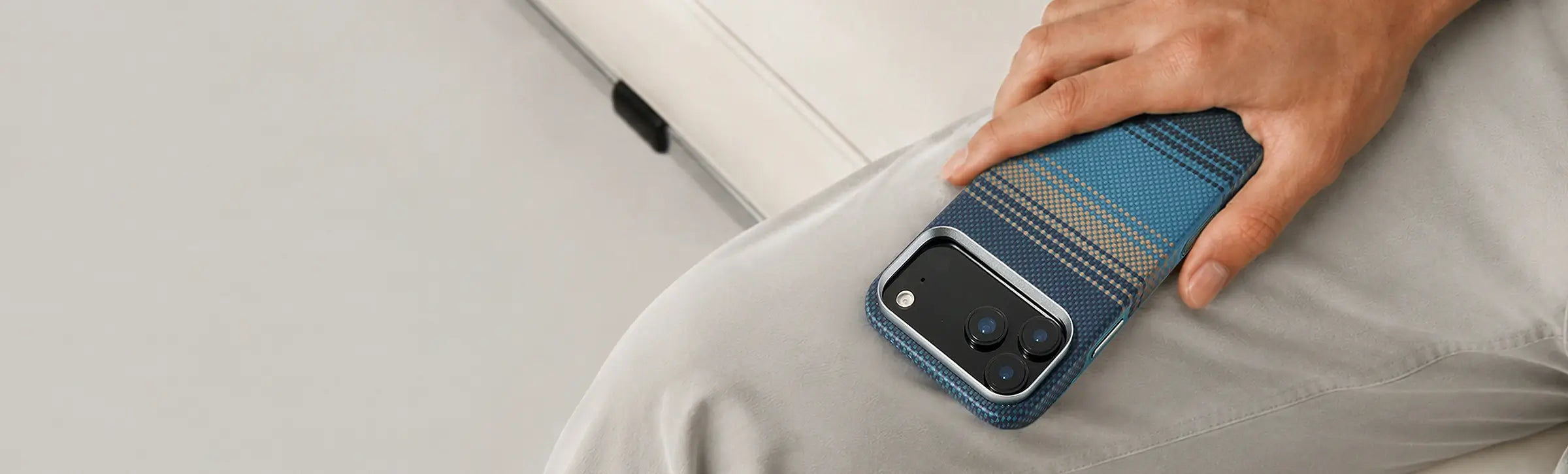 Blue textured iPhone case with striped fabric design placed on a person’s lap while being held by hand in a casual indoor setting.