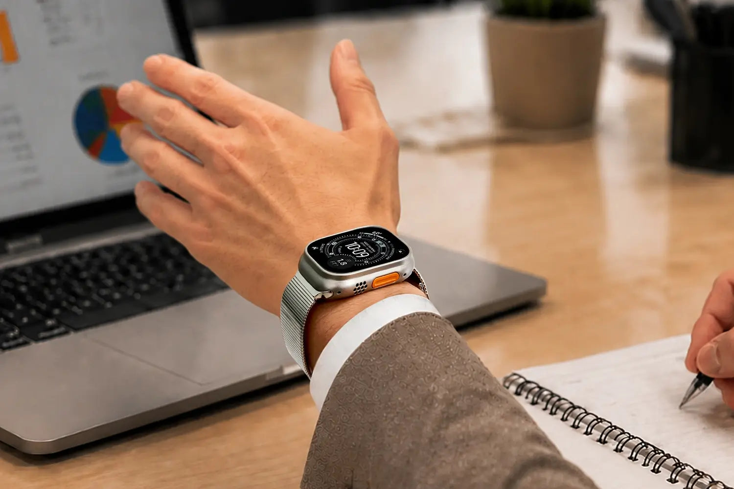 Person using a smartwatch with a laptop and notebook in the background