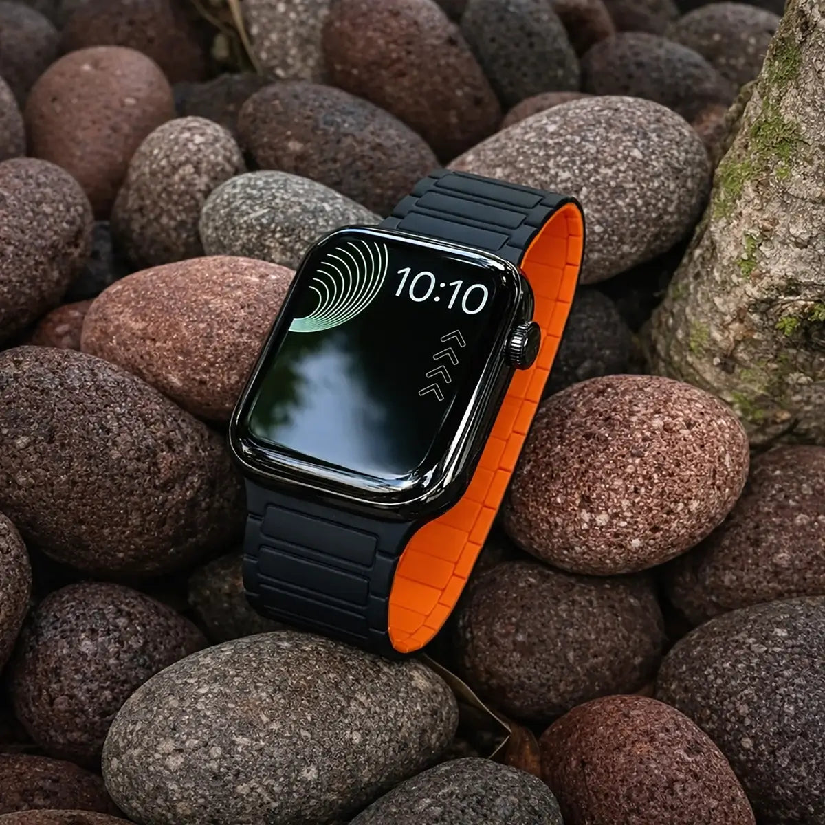 Smartwatch with a black and orange band on a bed of rocks