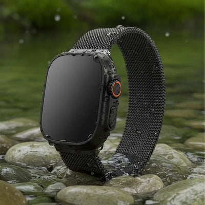 Smartwatch with a black mesh band on a rocky surface with water in the background