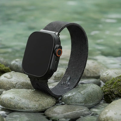 Smartwatch with a black mesh band on a stone surface with water in the background