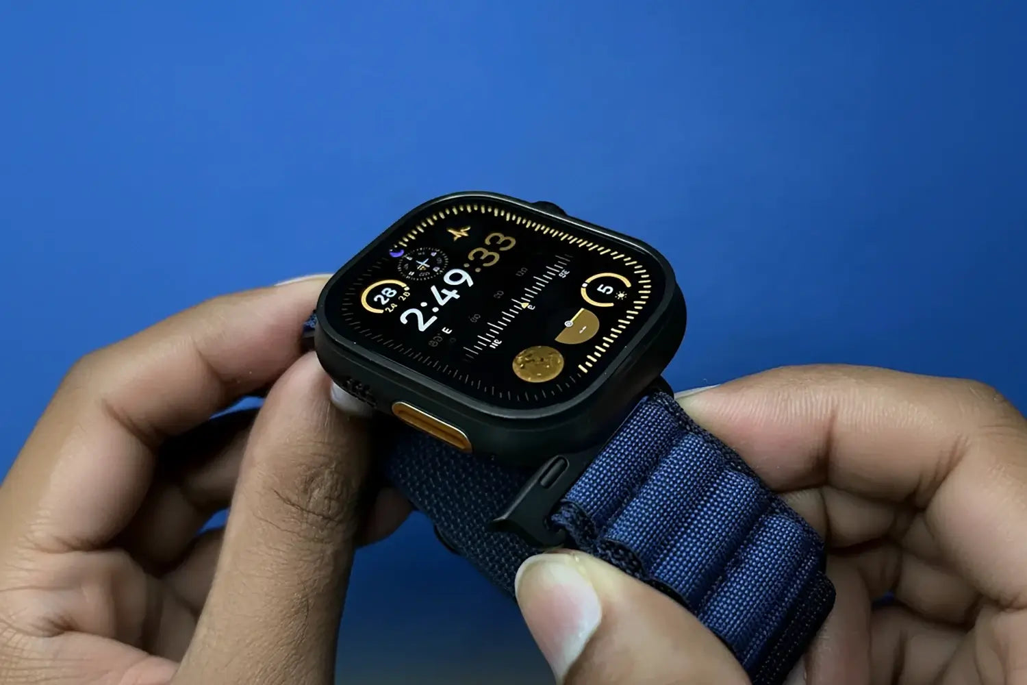 Smartwatch with a blue strap held in hands against a blue background