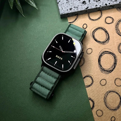 Watch with green strap on a green surface with a cardboard box in the background